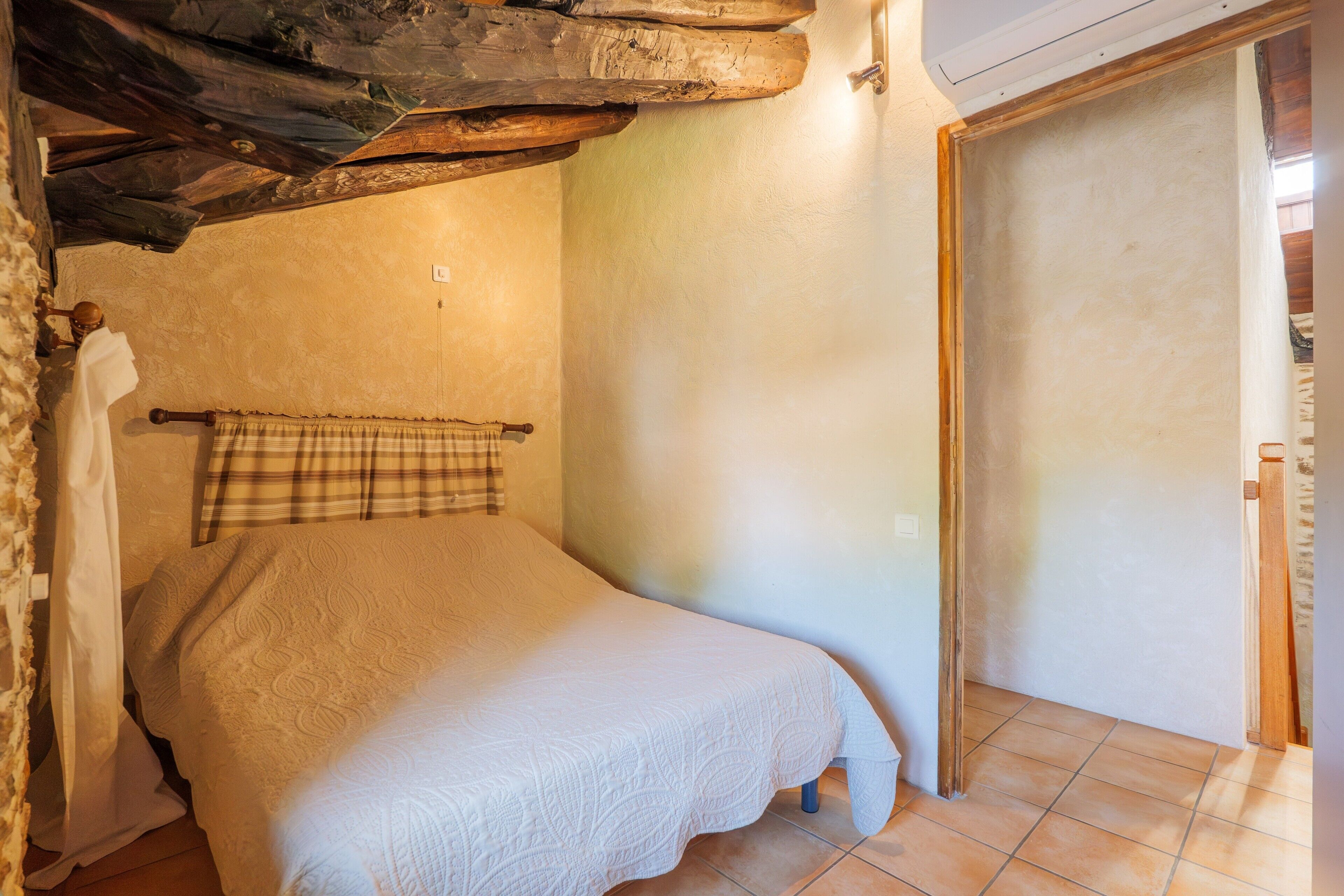 A bedroom with a bed, a wooden headboard, a window with a curtain, and a door.