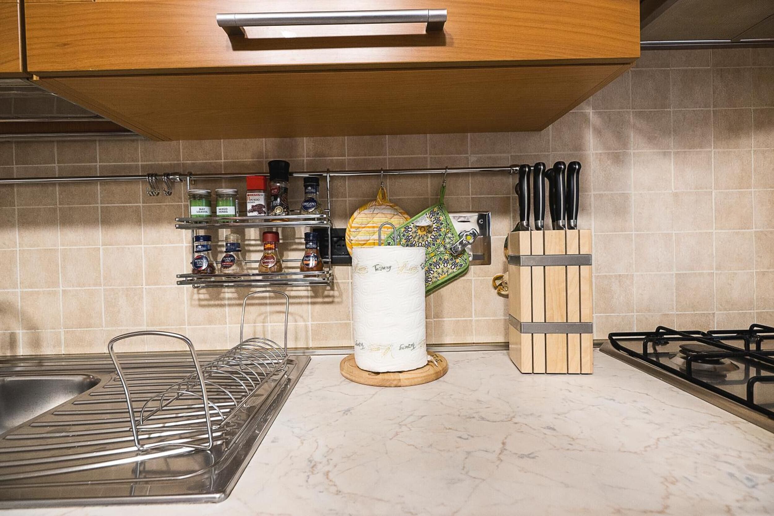 A kitchen with a gas stove, a hanging pot rack, and a spice rack.