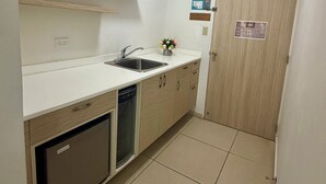 A compact kitchen with a sink, dishwasher, and wooden cabinets. - Caño Tiburones Guest House (Arecibo)