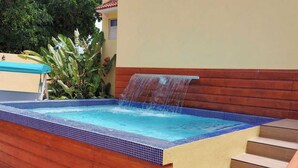 A hot tub with a waterfall feature, surrounded by wooden steps and a tiled edge. - Caño Tiburones Guest House (Arecibo)