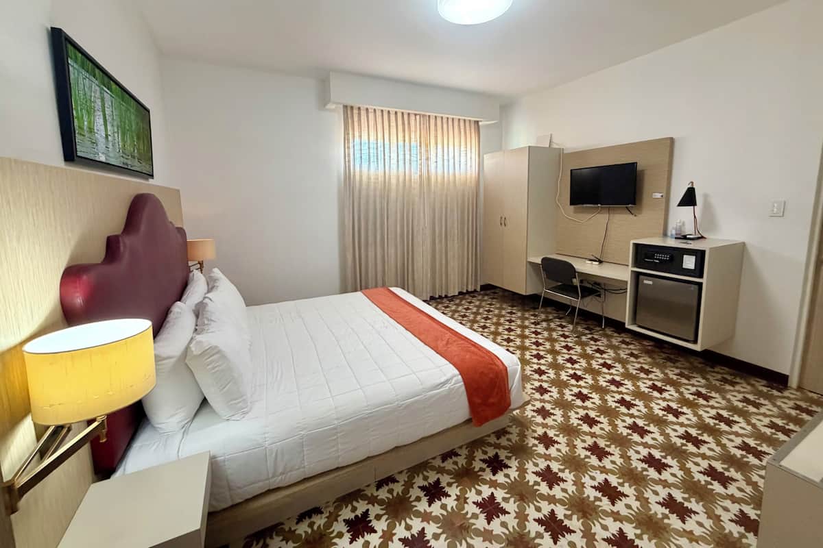 Una habitación de hotel con una cama, un escritorio, un televisor y un minibar.