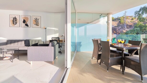A modern living room with a sofa, coffee table, and a dining area with wicker chairs and a glass table. - Seaview Splendor 2-BR luxury, huge terrace (Fuengirola)
