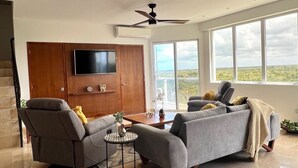 A spacious living room with a grey sofa, a small round table, and a flat-screen TV mounted on a wooden cabinet.