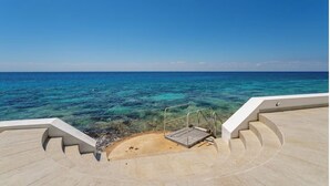 A view from a balcony overlooking a clear blue sea with a sandy beach and a metal railing.