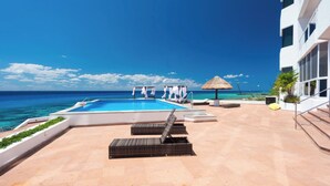 A pool area with lounge chairs, a thatched umbrella, and a view of the ocean.