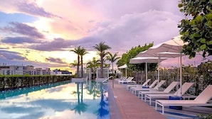 A swimming pool with lounge chairs and umbrellas, surrounded by greenery and buildings.