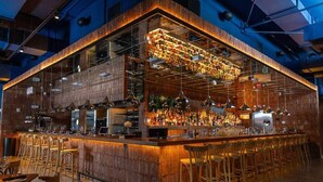 A bar with a wooden interior, multiple hanging lights, and a variety of bottles and glasses on shelves.