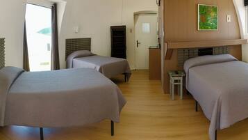 A room with two beds, a small table, a wooden cabinet, and a painting on the wall.