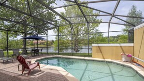 A covered outdoor swimming pool with a view of a lake, surrounded by chairs and a table. - EV_3169 - 4 Bed 3.5 Bath Townhome with Screened-In Private Pool (Kissimmee)