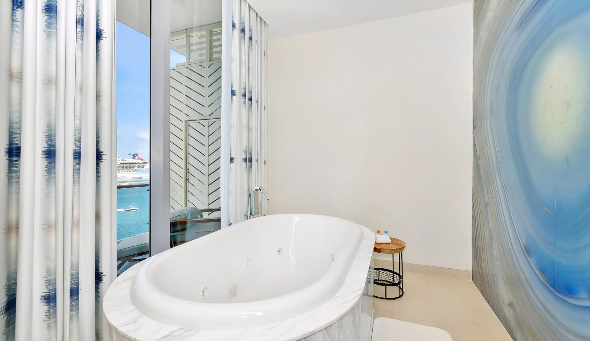A modern bathroom with a freestanding bathtub, a glass shower enclosure, and a view of a cruise ship.