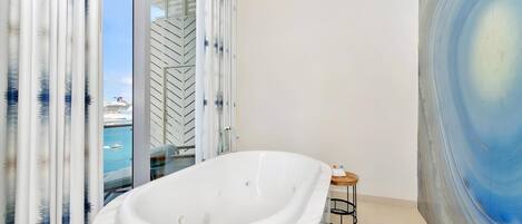 A modern bathroom with a freestanding bathtub, a glass shower enclosure, and a view of a cruise ship.
