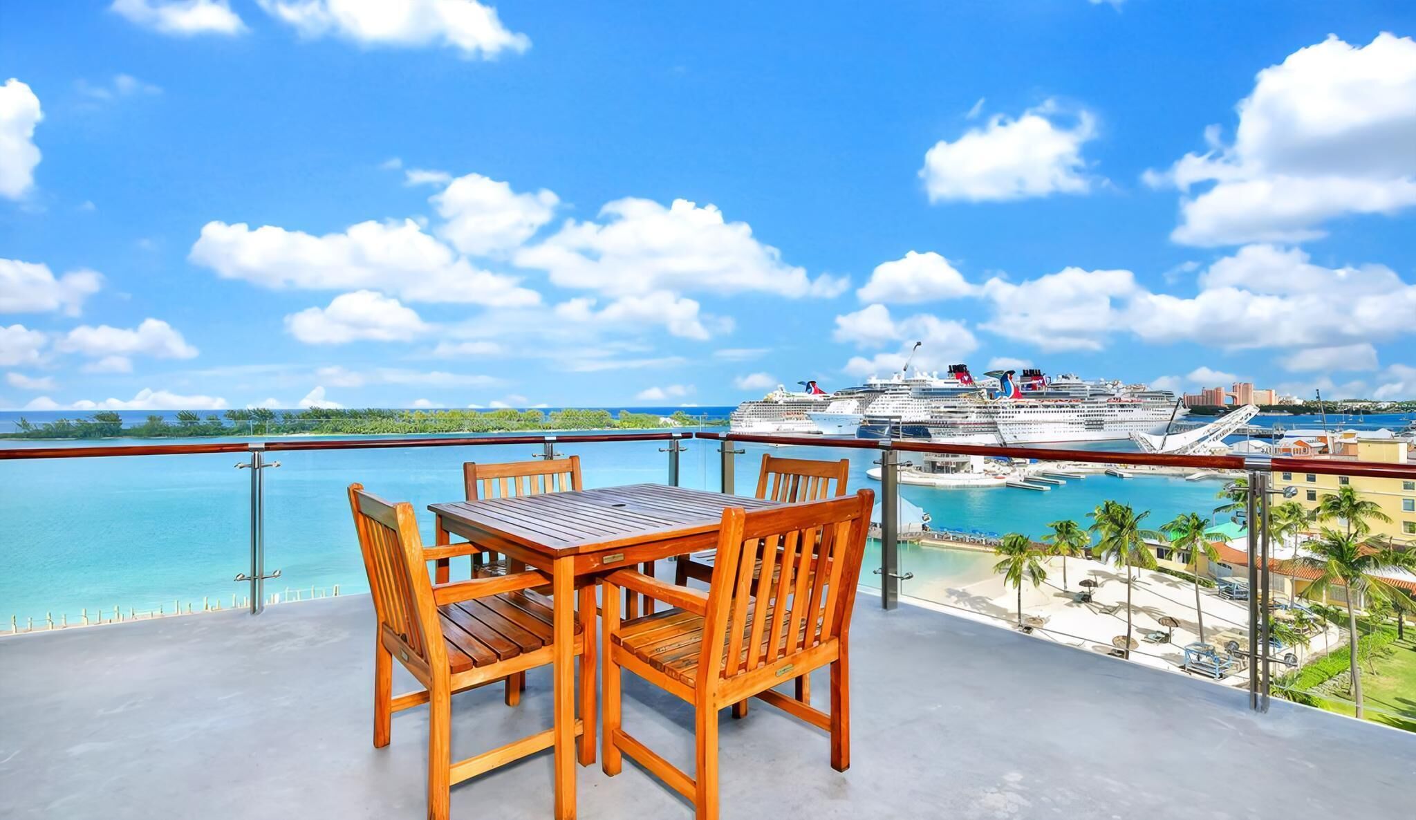 Une table et des chaises en bois sur un balcon donnant sur un navire de croisière et une plage.