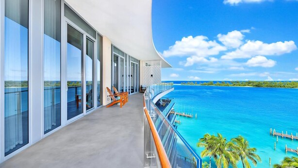 A modern balcony with glass doors, a pool, and a view of the ocean.