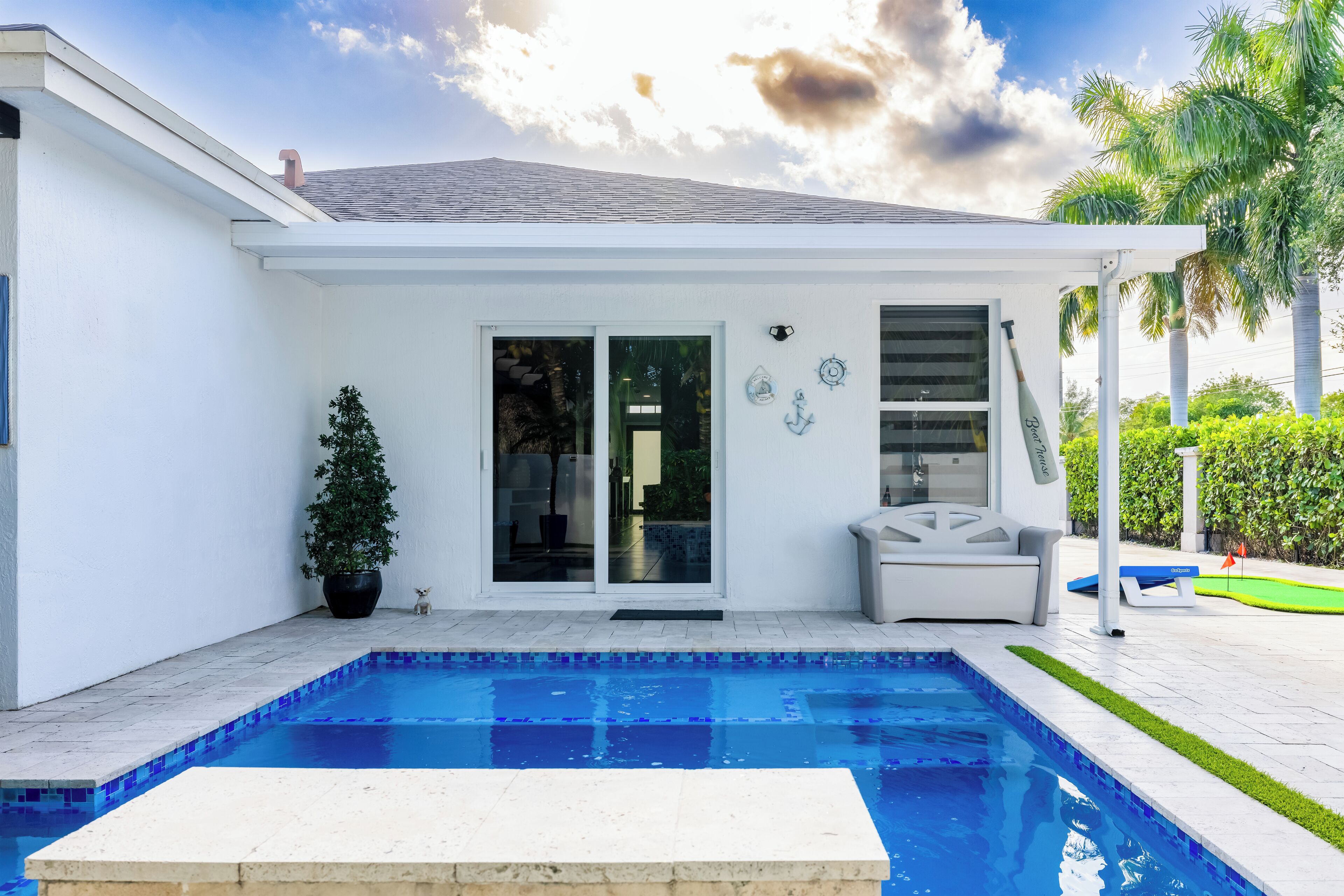 A modern house with a swimming pool, a patio with a lounge chair, and a small garden area.