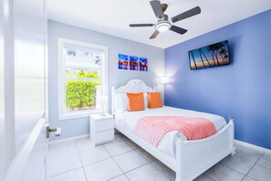 A bedroom with a bed, nightstand, ceiling fan, window, and artwork on the wall.