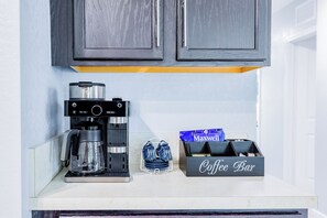 A coffee maker, a coffee bar sign, and Maxwell's coffee bags on a kitchen counter.