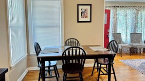 A dining area with a wooden table and chairs, a framed picture on the wall, and a red door in the background. - The Pedal Pad - 3 BED / 1 BATH @ central location (Wichita Falls)