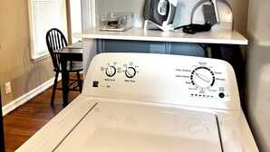 A laundry area with a front-loading washer and dryer, a small table with a broom and a framed picture on the wall. - The Pedal Pad - 3 BED / 1 BATH @ central location (Wichita Falls)