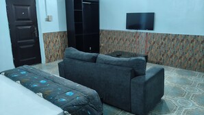 A room with a bed, a sofa, a television on the wall, and a patterned floor. - Oasis Place (Port Harcourt)