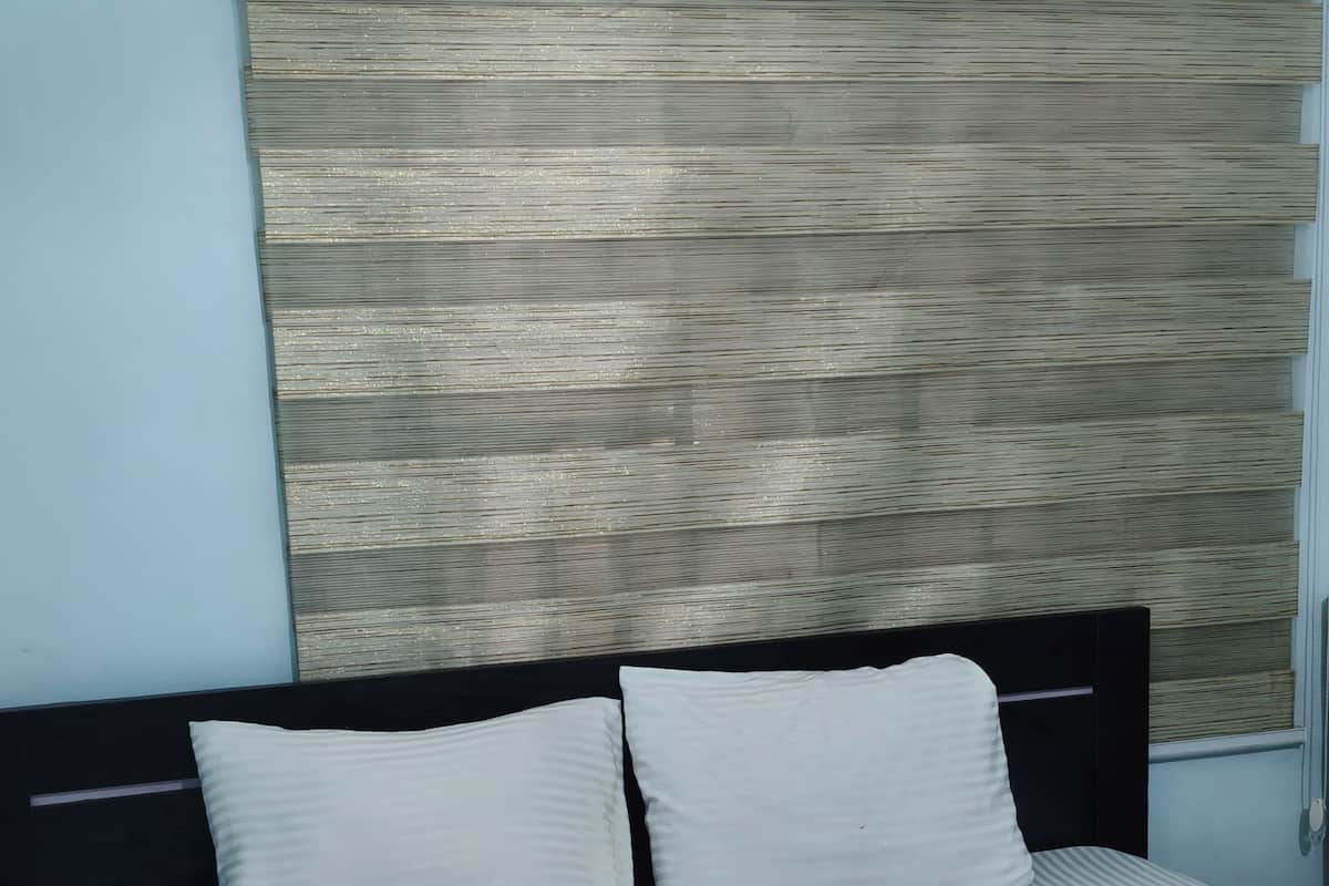 Una cama con colcha a rayas y manta de estampado de hojas verdes, cabecero negro y cabecera de pared texturizada.