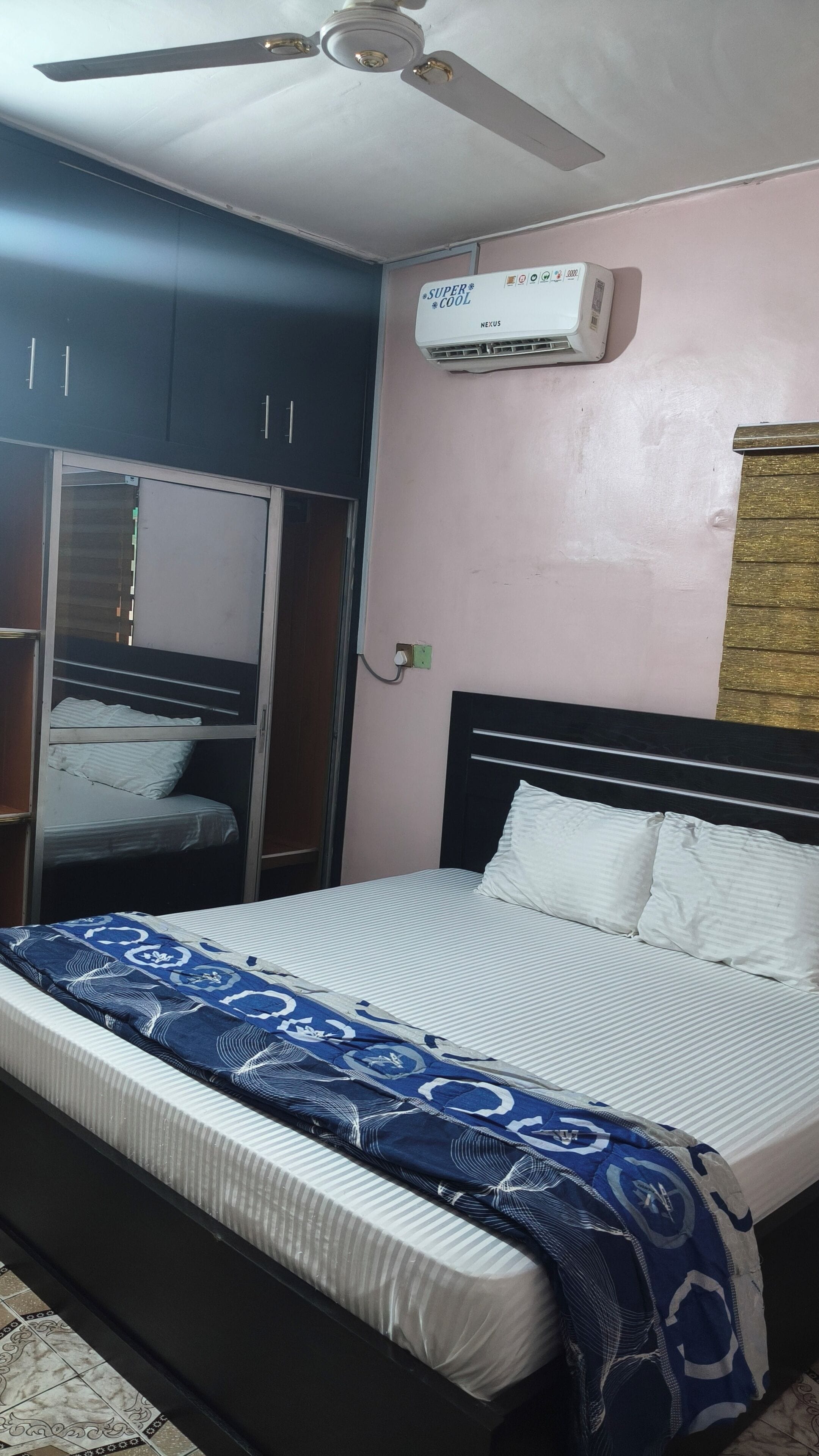 A bedroom with a bed, a ceiling fan, a wardrobe, and an air conditioning unit.