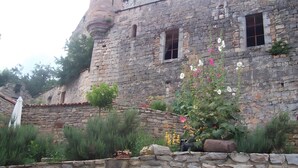 Un edificio de piedra con una torre, ventanas y un jardín con plantas y flores.