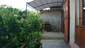 Una terraza de madera que lleva a un patio cubierto con un muro de piedra y una mesa de madera.