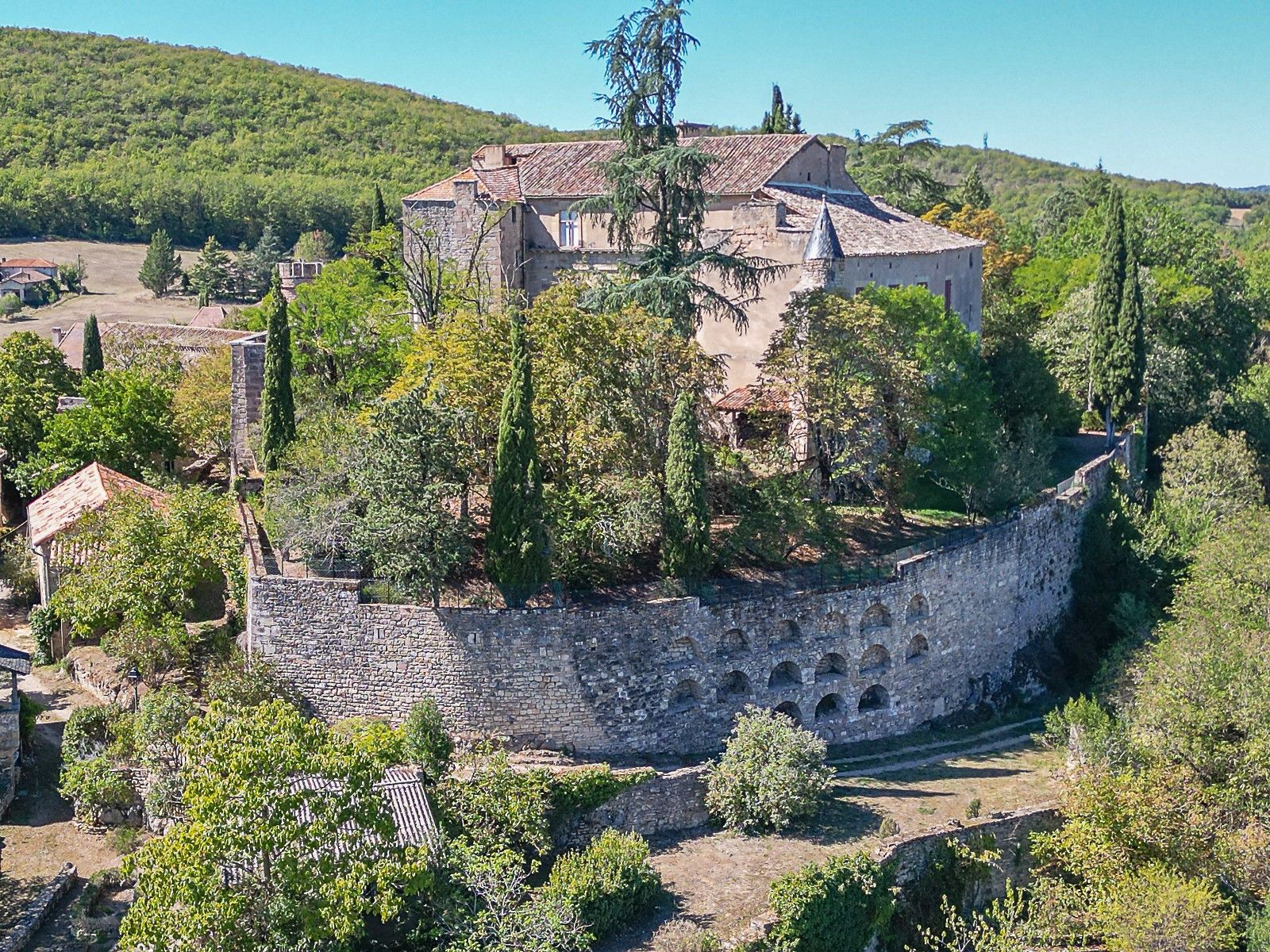 Um edifício de pedra histórico com uma torre, rodeado por árvores e um muro de pedra.