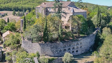 Um edifício de pedra histórico com uma torre, rodeado por árvores e um muro de pedra.