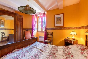 A bedroom with a bed, a nightstand, a lamp, a chair, a mirror, and a window with curtains.
