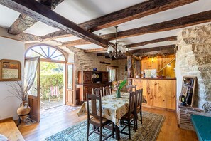A rustic dining area with a wooden table and chairs, a chandelier, and a stone wall.
