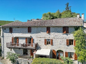 A two-story stone building with a balcony, wooden shutters, and a tiled roof.