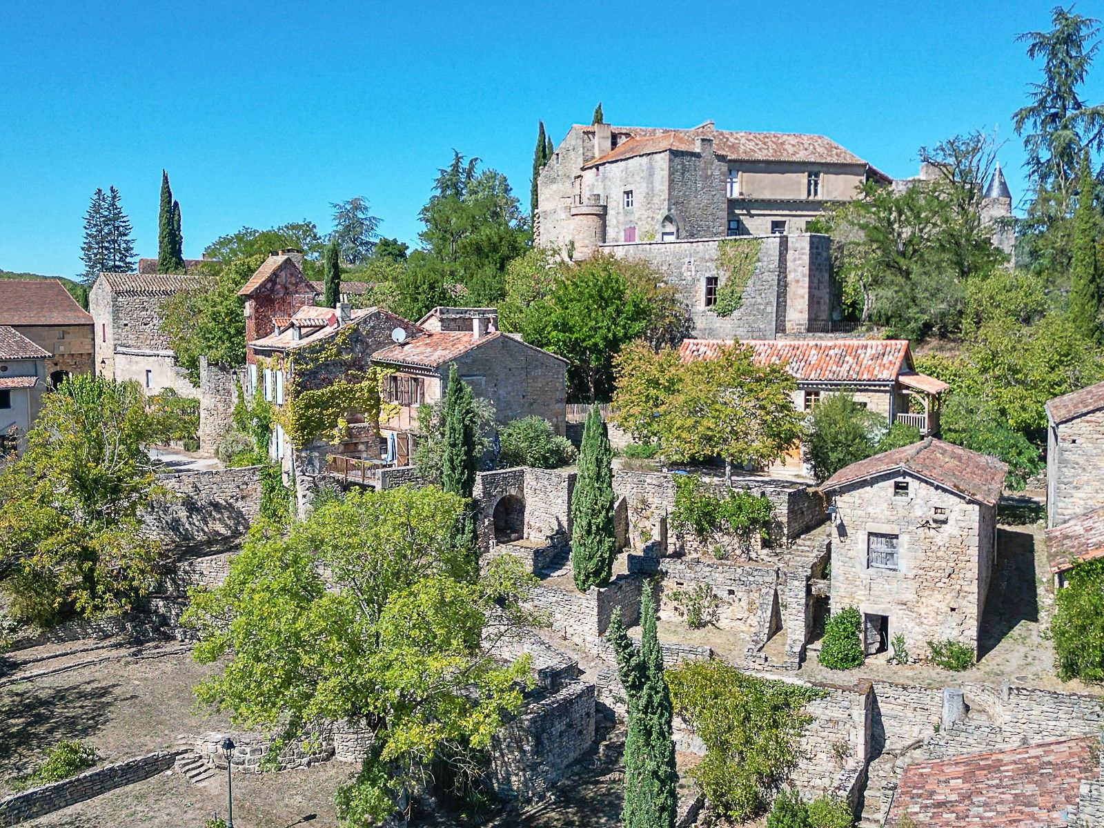 A historic stone building with a traditional roof, surrounded by trees and other stone structures.
