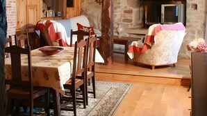 Un interior rústico con vigas de madera a la vista, una chimenea de piedra, una mesa de comedor con sillas y una alfombra estampada.