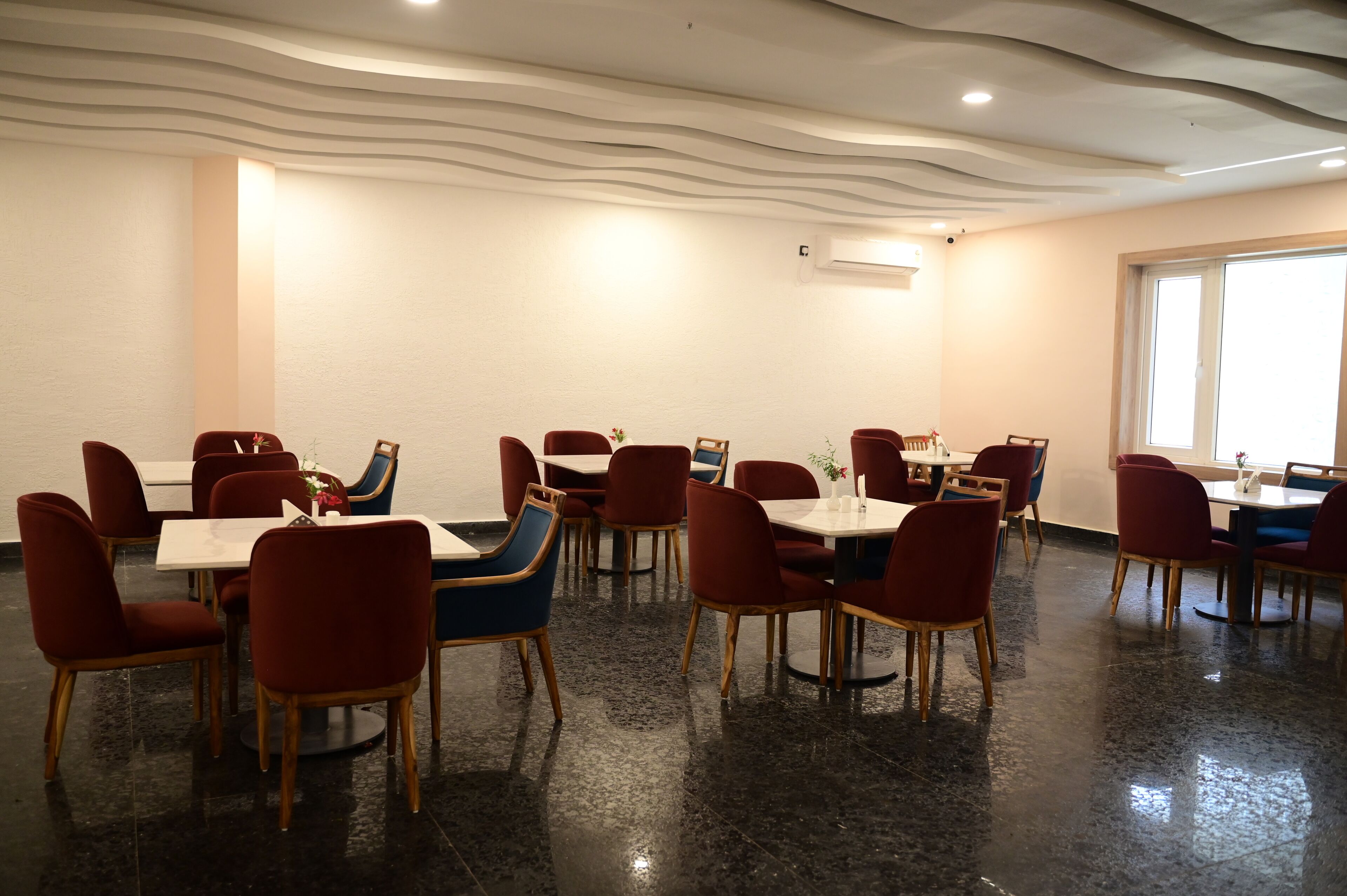 Un espace repas avec des tables et des chaises, un plafond au motif ondulé et une fenêtre sur le côté droit.