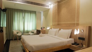 A hotel room with a wooden bed, a desk with a chair, a small table, and a telephone.