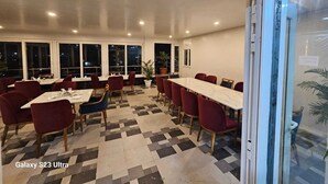 A restaurant with a long table and red chairs, a patterned floor, and large windows.