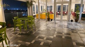 A terrace with green chairs and a table, potted plants, and a view of the city at night.