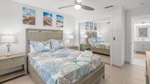 Ein Schlafzimmer mit Bett, Nachttischen, Deckenventilator und Kunstwerken an den Wänden.