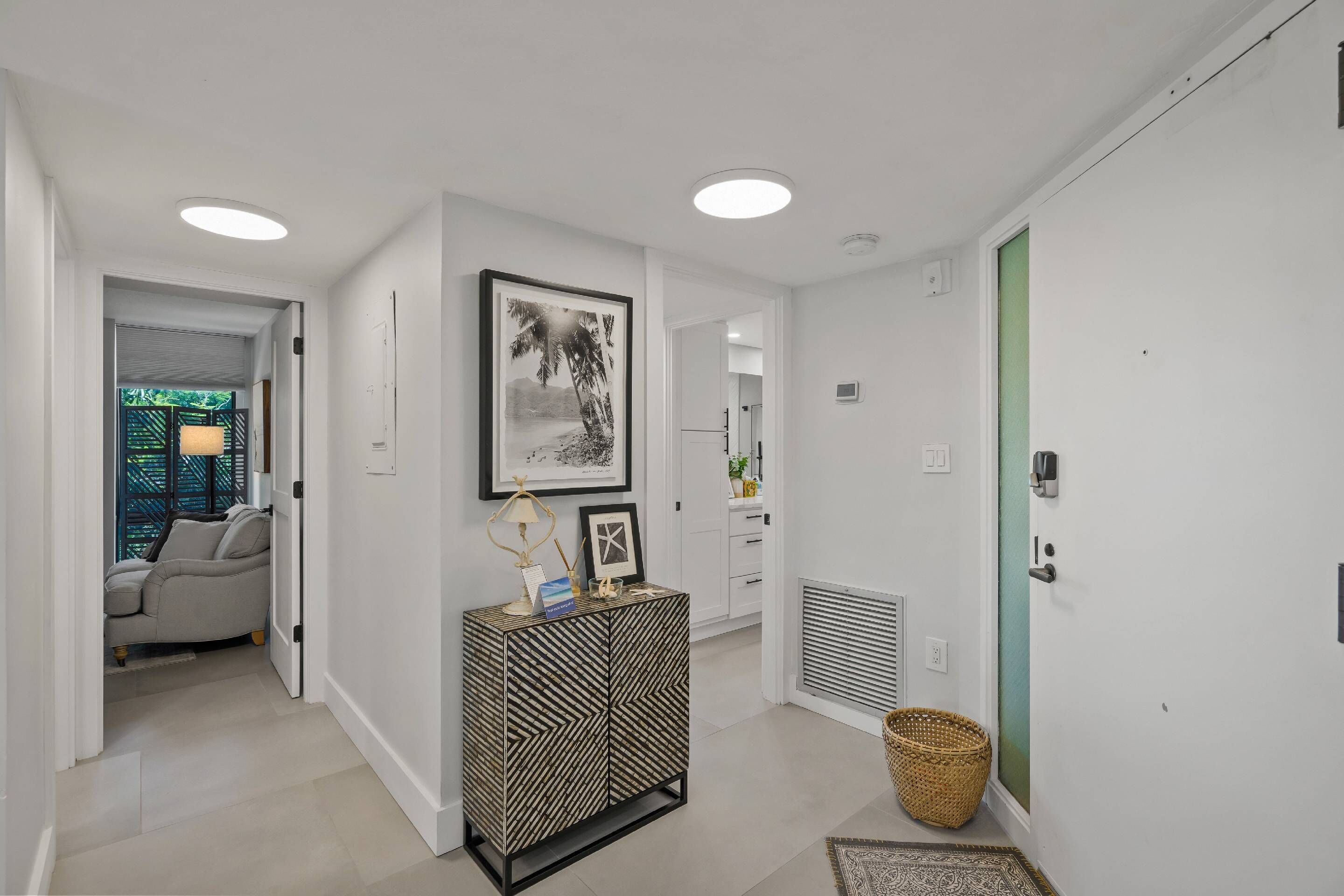 A hallway with a sofa, a console table with a framed picture, a basket, and a door with a green panel.