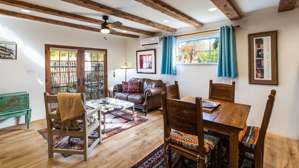Ein gemütliches Wohnzimmer mit Holzbalkendecke, einem braunen Ledersofa, einem Holzesstisch mit Stühlen und einem gemusterten Teppich.