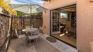 Eine Terrasse mit Tisch und Stühlen, einem gestreiften Sonnenschirm und einem Holzzaun.