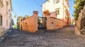 Une ruelle pavée étroite, bordée de bâtiments historiques dotés d’arcades et d’une entrée fermée par un portail.