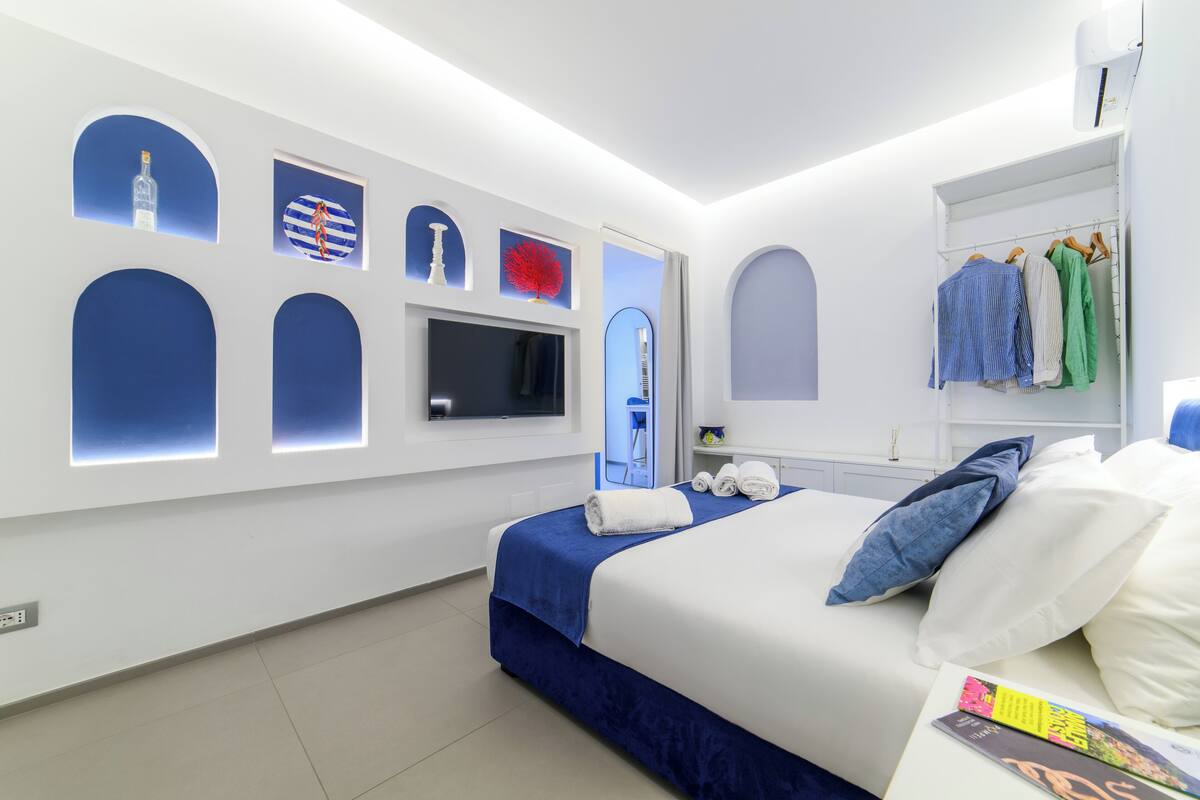 A modern hotel room with a neatly made bed, a television, a wardrobe, and a mirror.