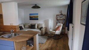 A compact living space with a kitchenette, a sofa, a rocking chair, and a bookshelf.