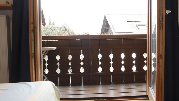 A room with a wooden floor, a bed with a striped bedspread, and a balcony with a wooden railing and decorative elements.