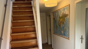 A wooden staircase with a white handrail leading to a landing. A hallway extends from the landing with a large world map on the wall.