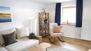 A living room with a sofa, a rocking chair, a wooden bookshelf, and a window with curtains.