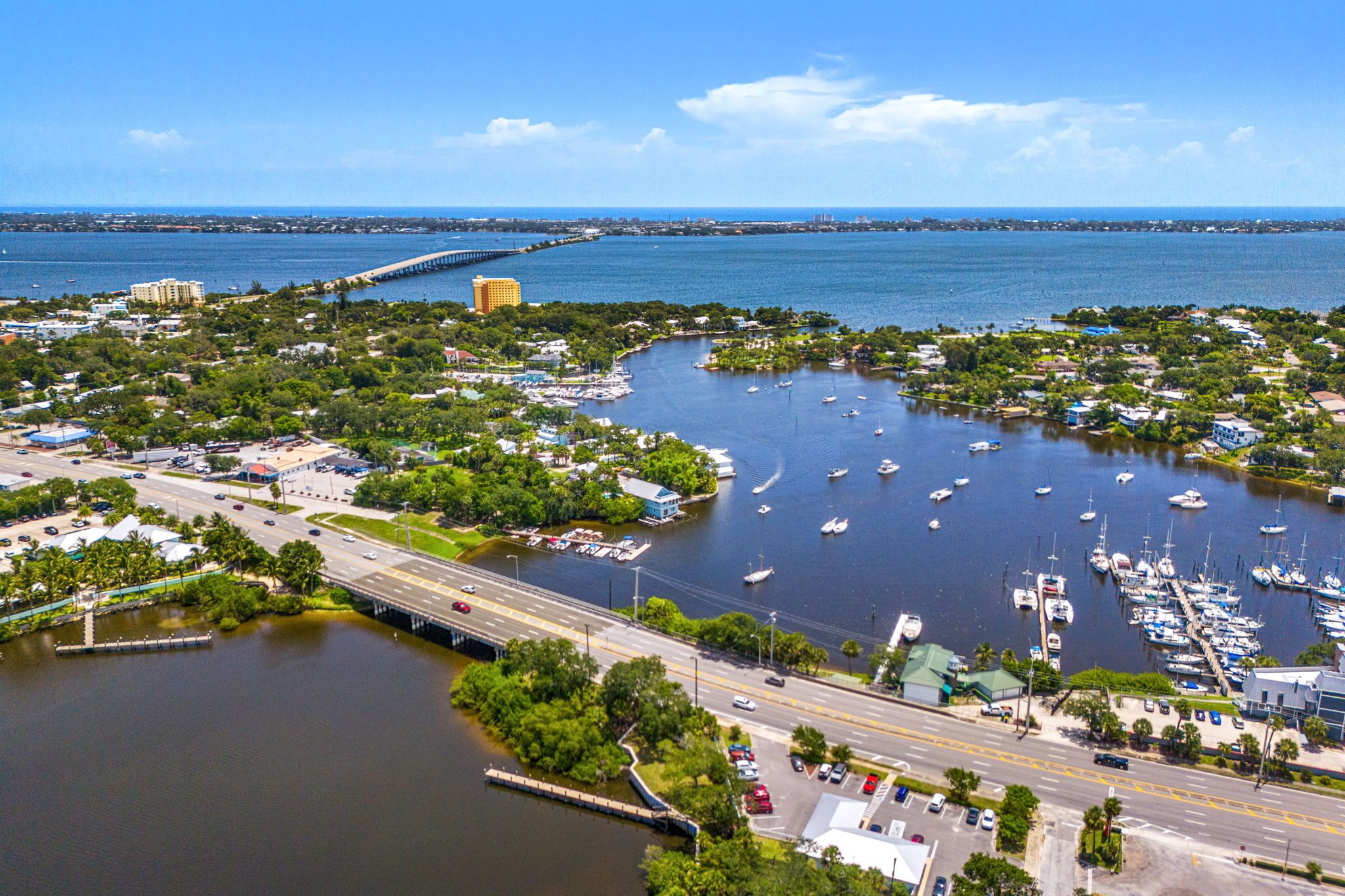 An aerial view of a marina with boats, a bridge, and surrounding greenery.