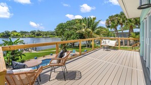 A wooden deck with outdoor furniture, a pool, and a view of a lake and palm trees. - Mango Shores (Melbourne)
